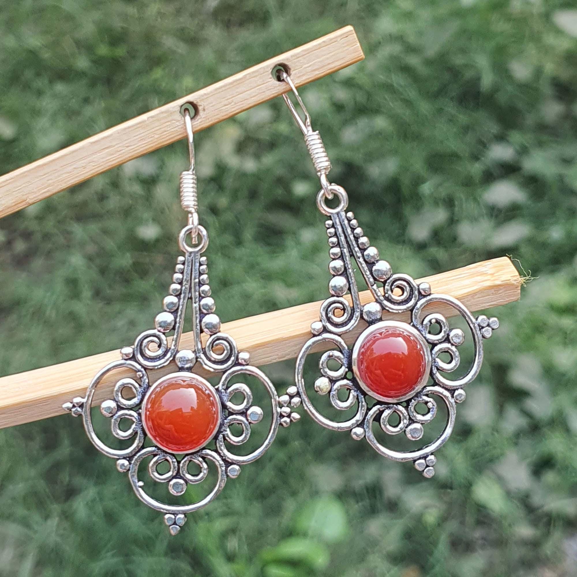 Silver earrings with red stones on a wooden stick against a green background