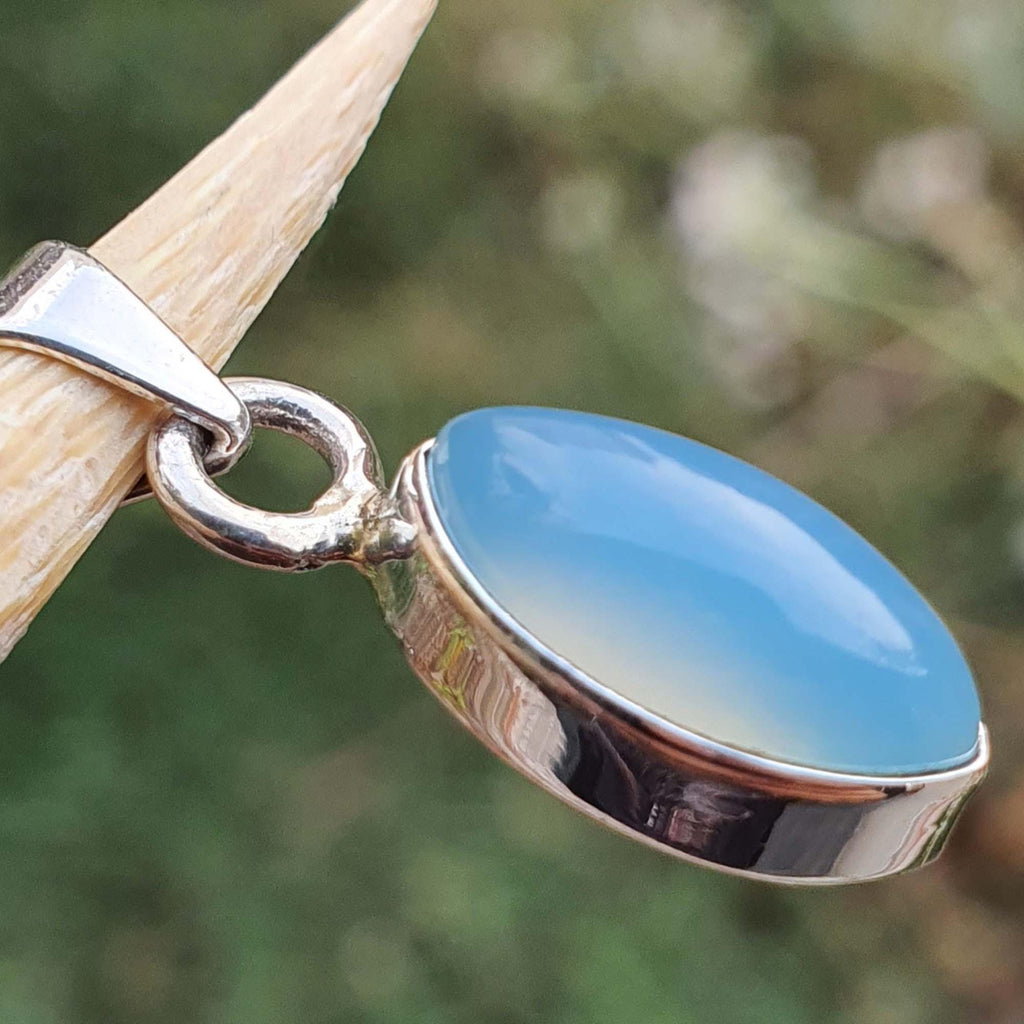Blue pendant with silver setting on a blurred natural background