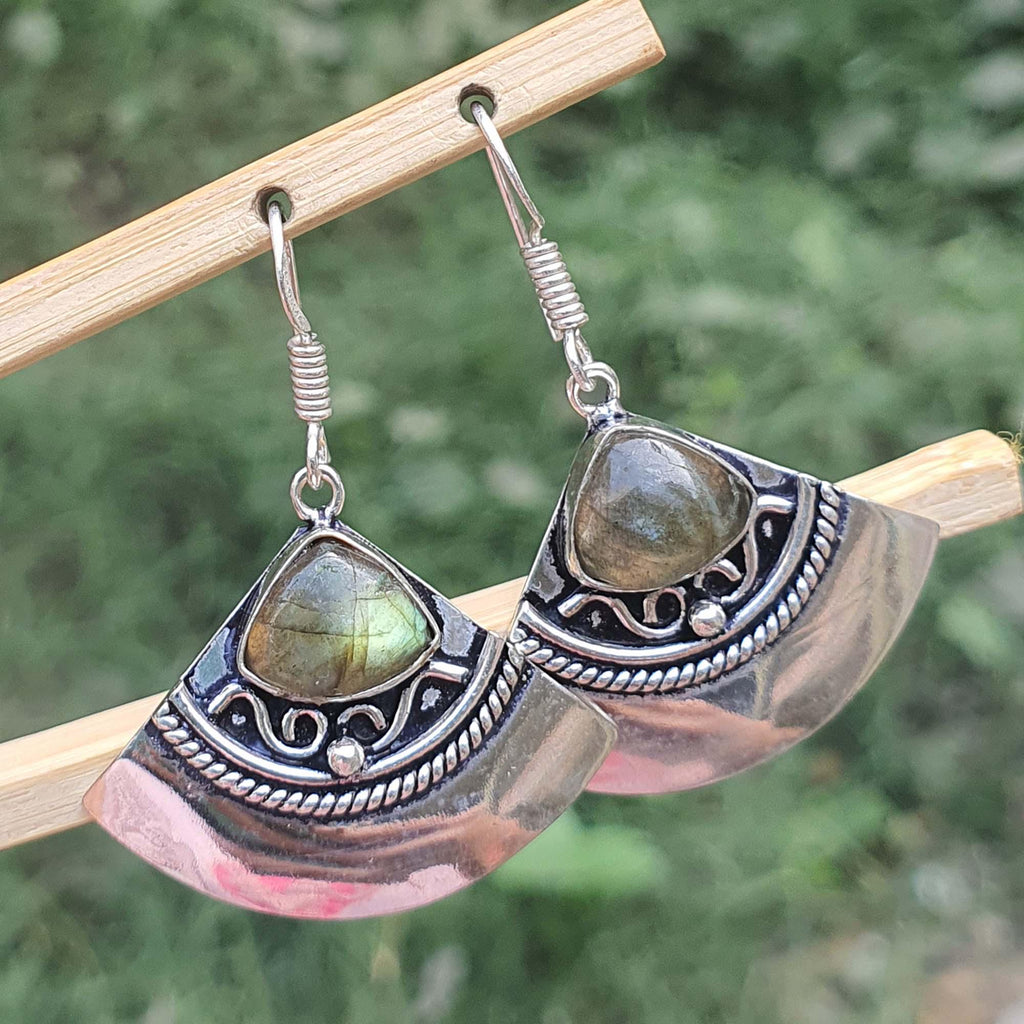 Silver earrings with green gemstones on a wooden stick against a blurred natural background