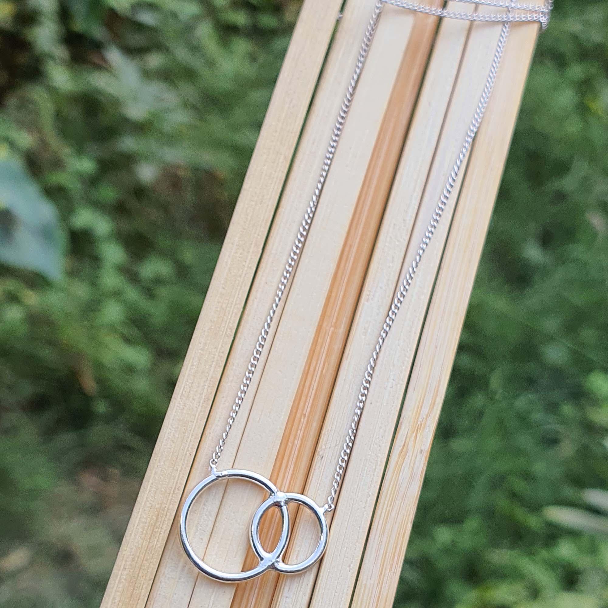 Silver necklace with interlocking rings on a wooden stick against a blurred green background