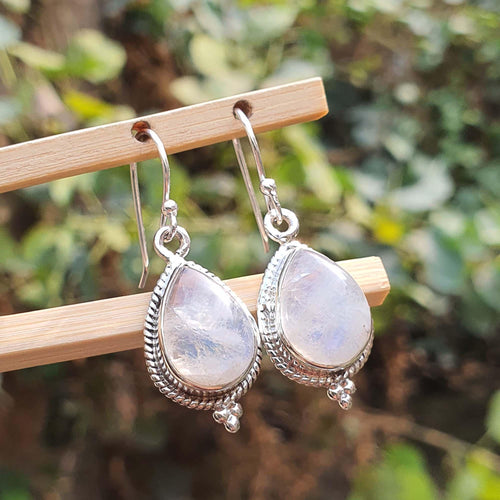 Silver earrings with teardrop-shaped gemstones on a wooden stick against a blurred natural background