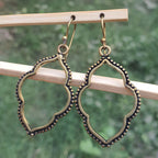 Pair of gold and black earrings hanging on a wooden stick with a green blurred background