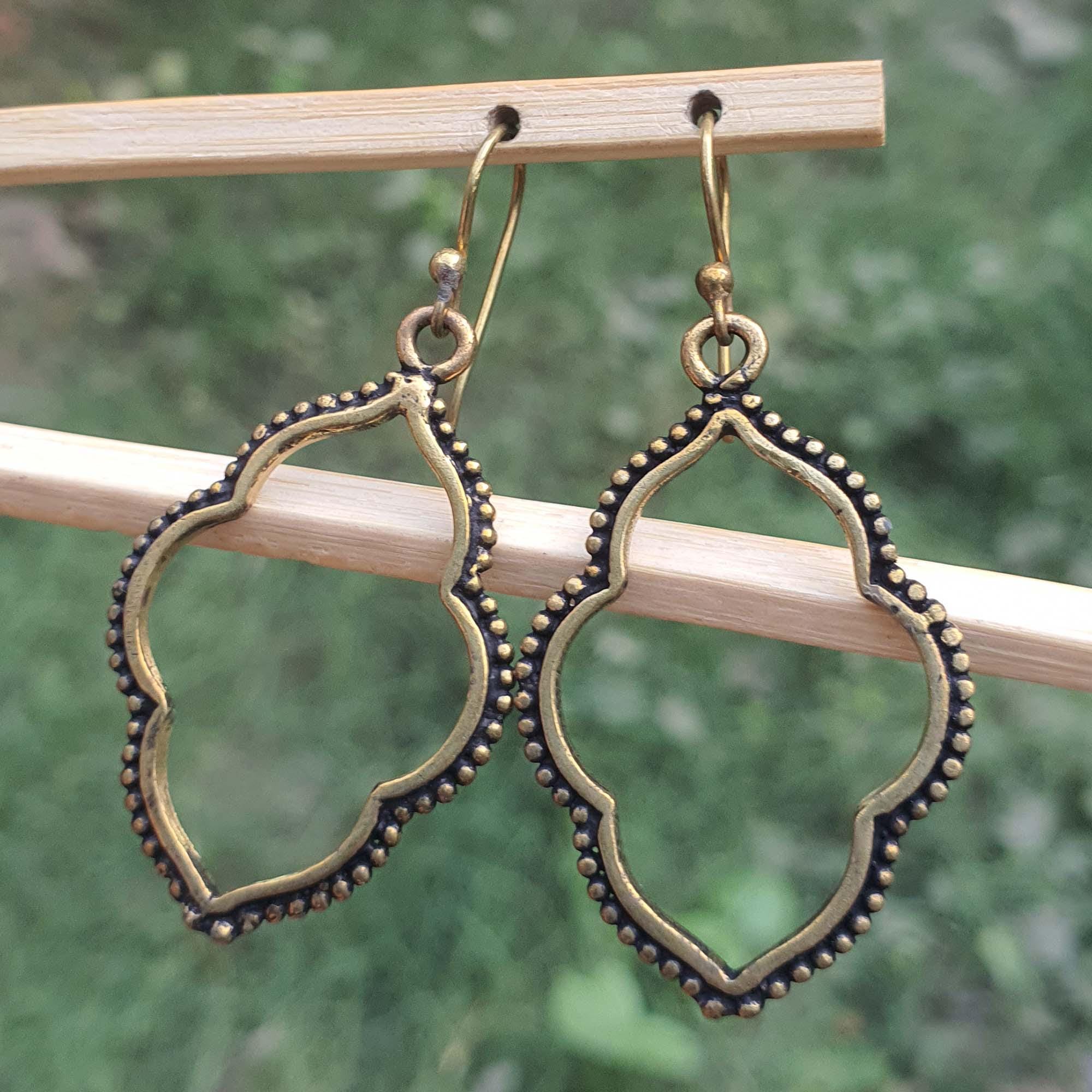 Pair of gold and black earrings hanging on a wooden stick with a green blurred background