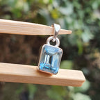 Silver pendant with a blue gemstone on a wooden stick against a blurred natural background