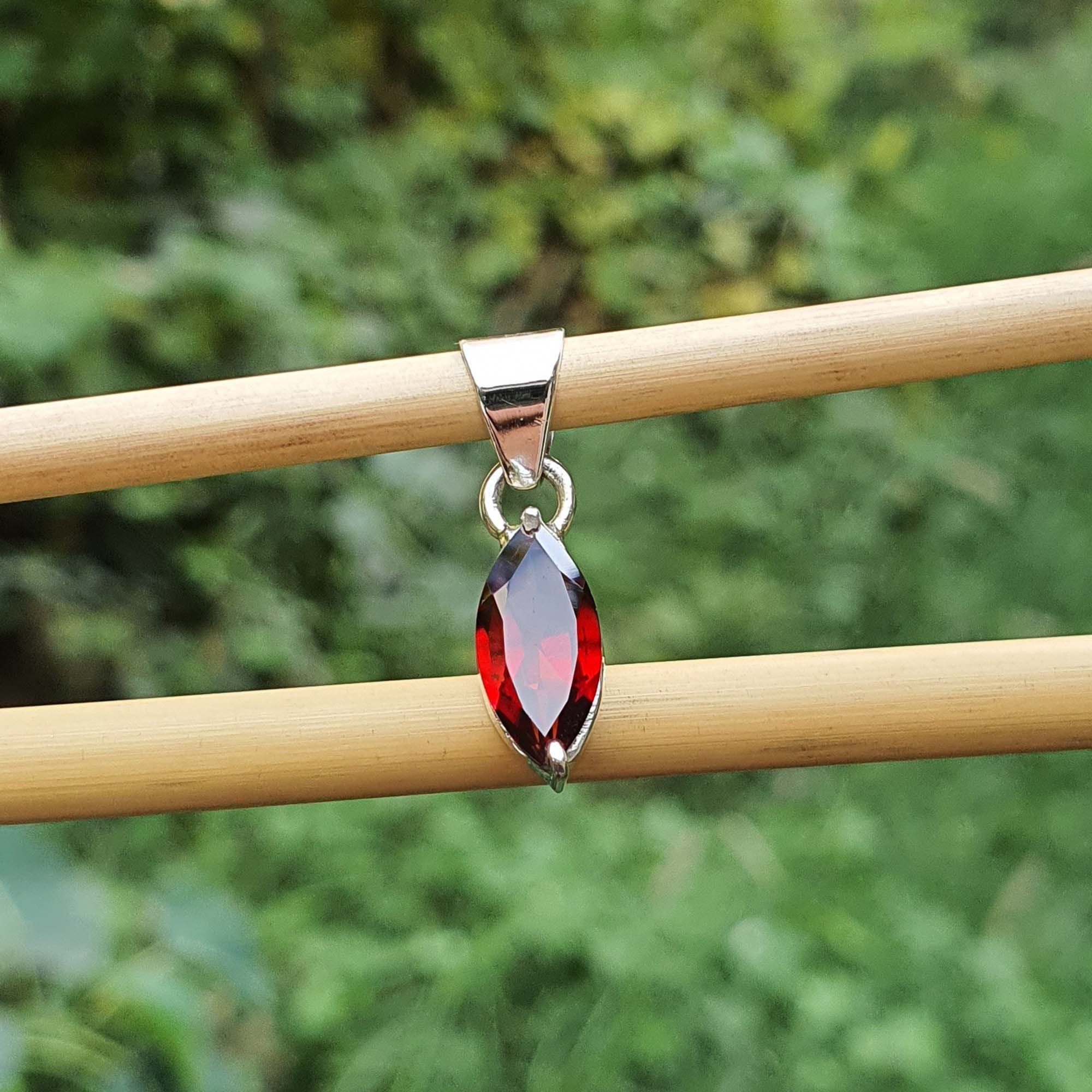 Silver pendant with a red gemstone on a wooden stick against a green background