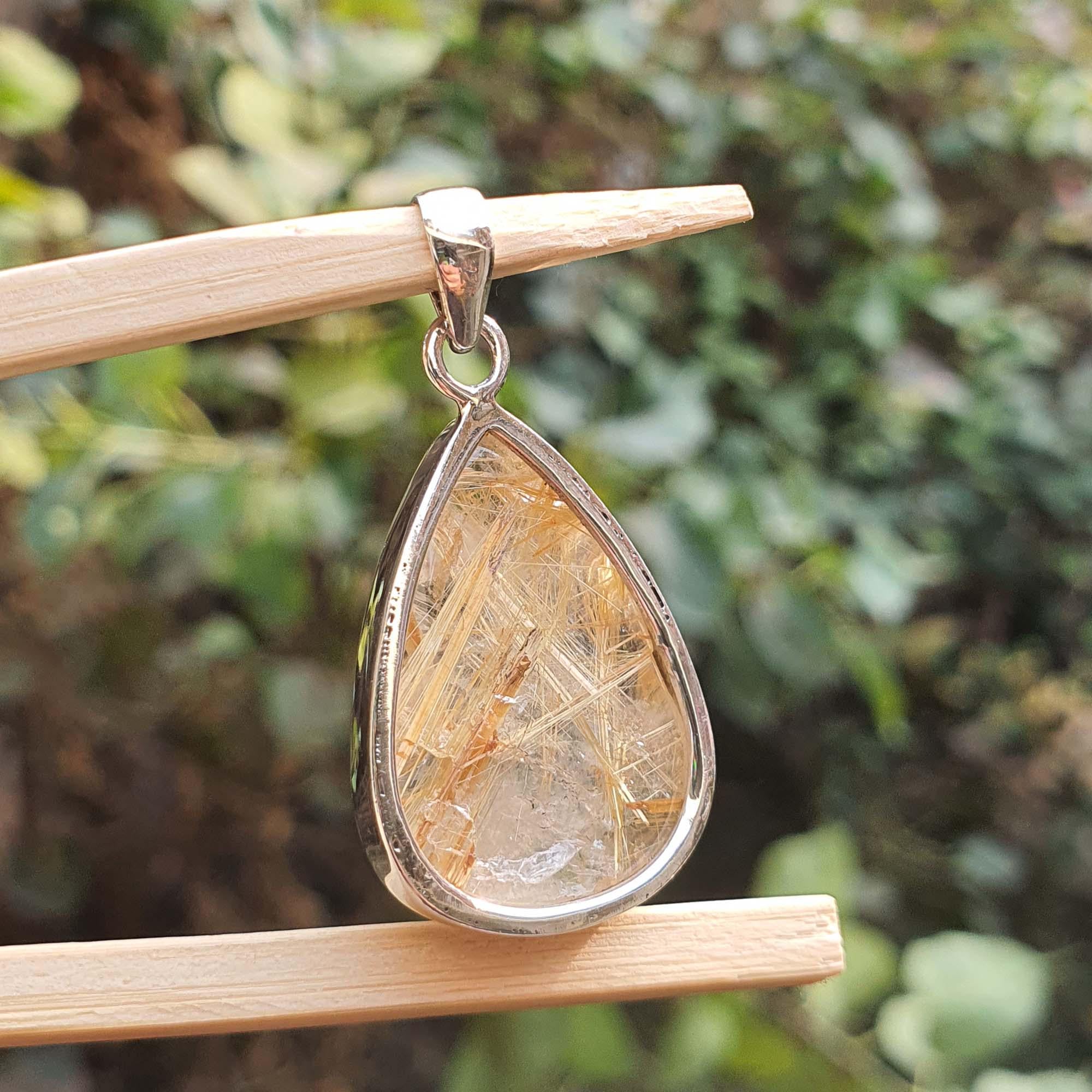 Teardrop-shaped crystal pendant on a wooden stick with a blurred green background