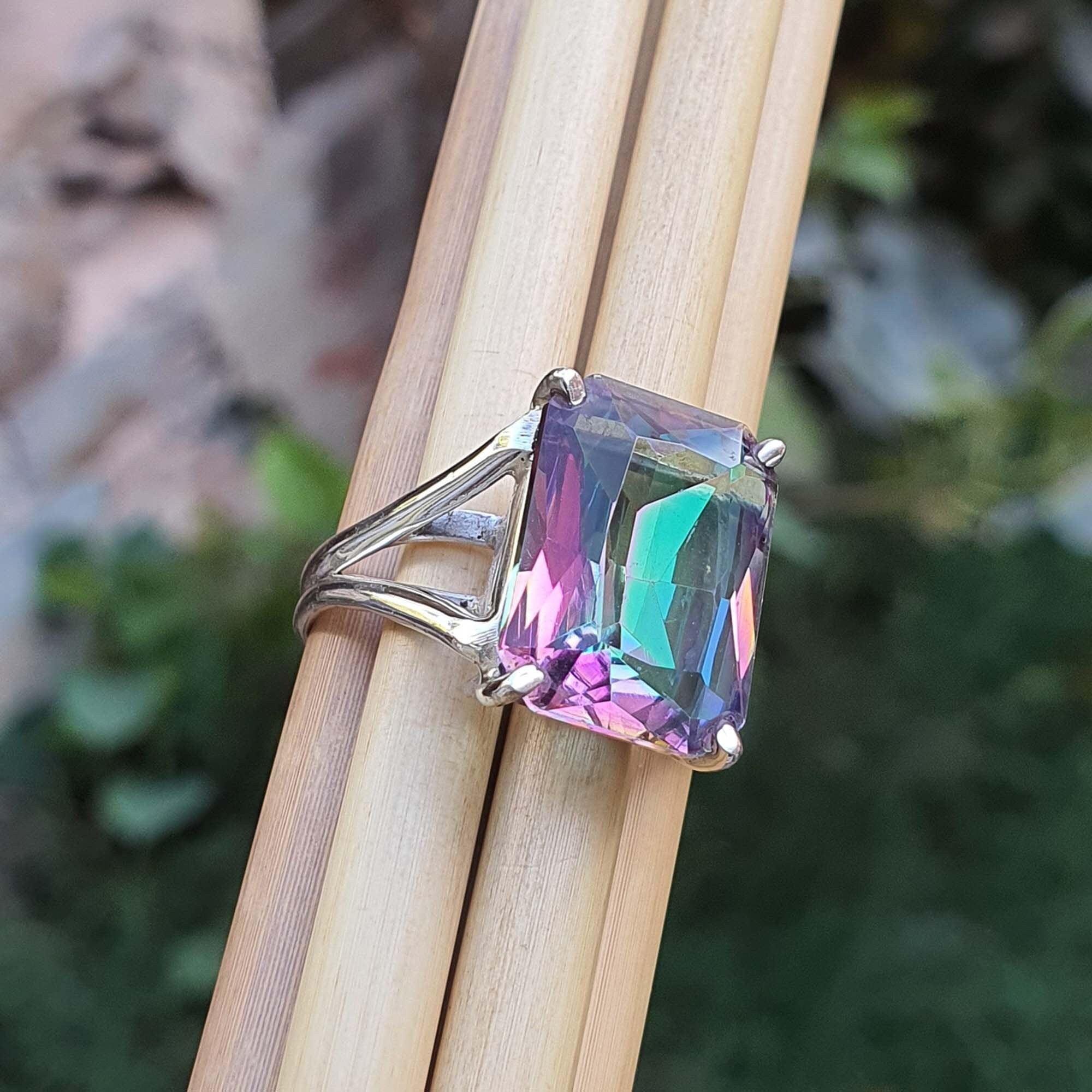 Ring with a colorful gemstone held between two sticks against a natural background