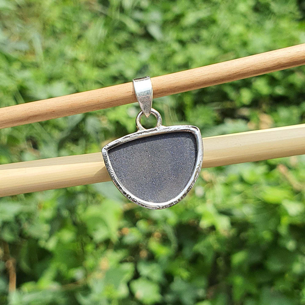 Silver pendant with a dark stone on a stick against a green leafy background