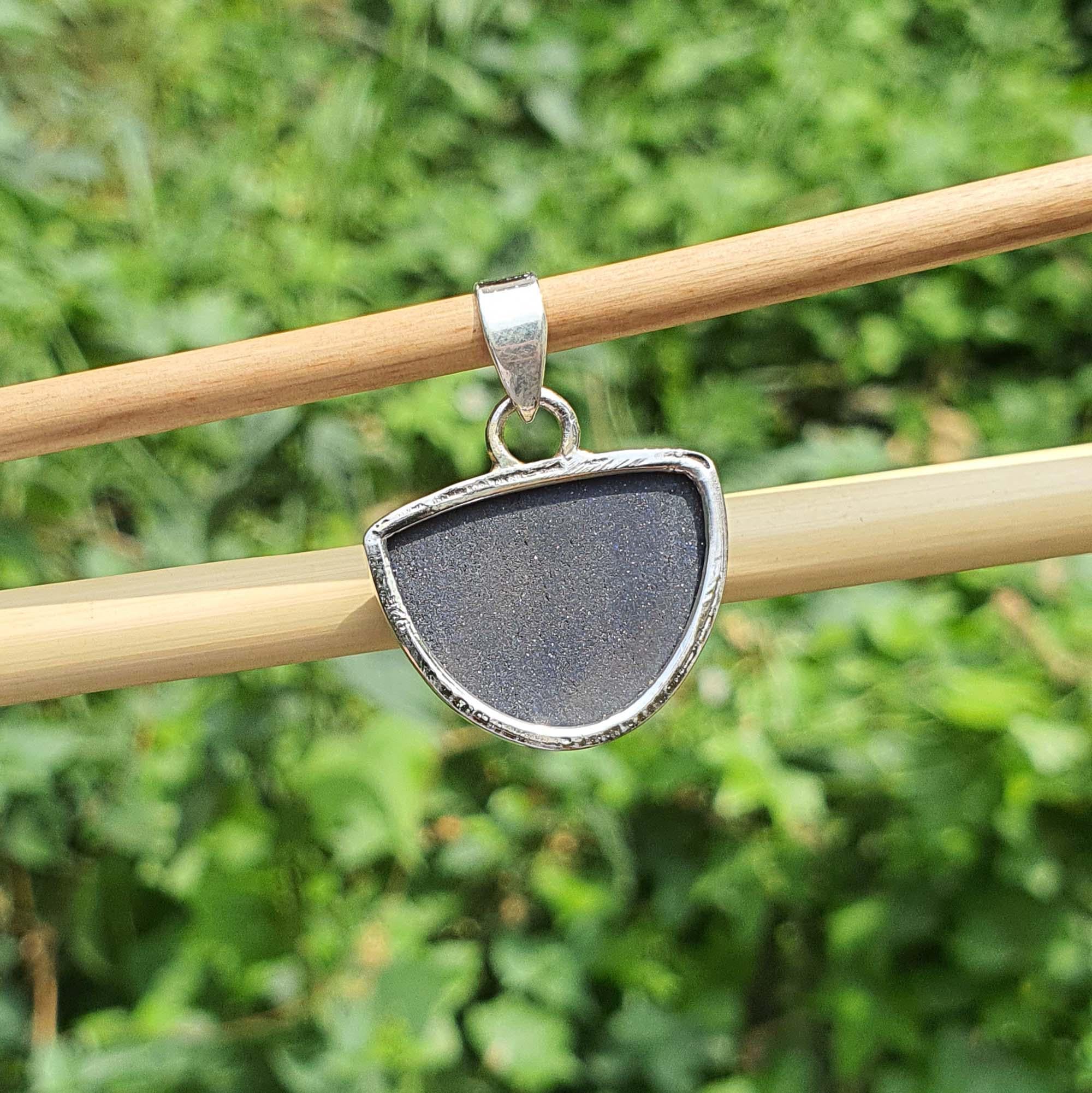 Silver pendant with a dark stone on a stick against a green leafy background