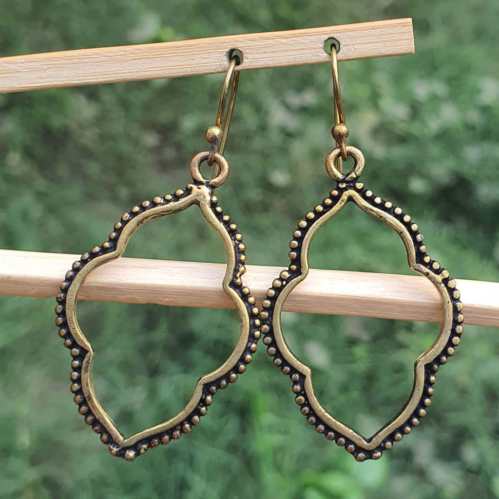 Pair of gold and black earrings hanging on a wooden stick with a green blurred background