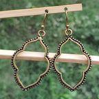 Pair of gold and black earrings hanging on a wooden stick with a green blurred background