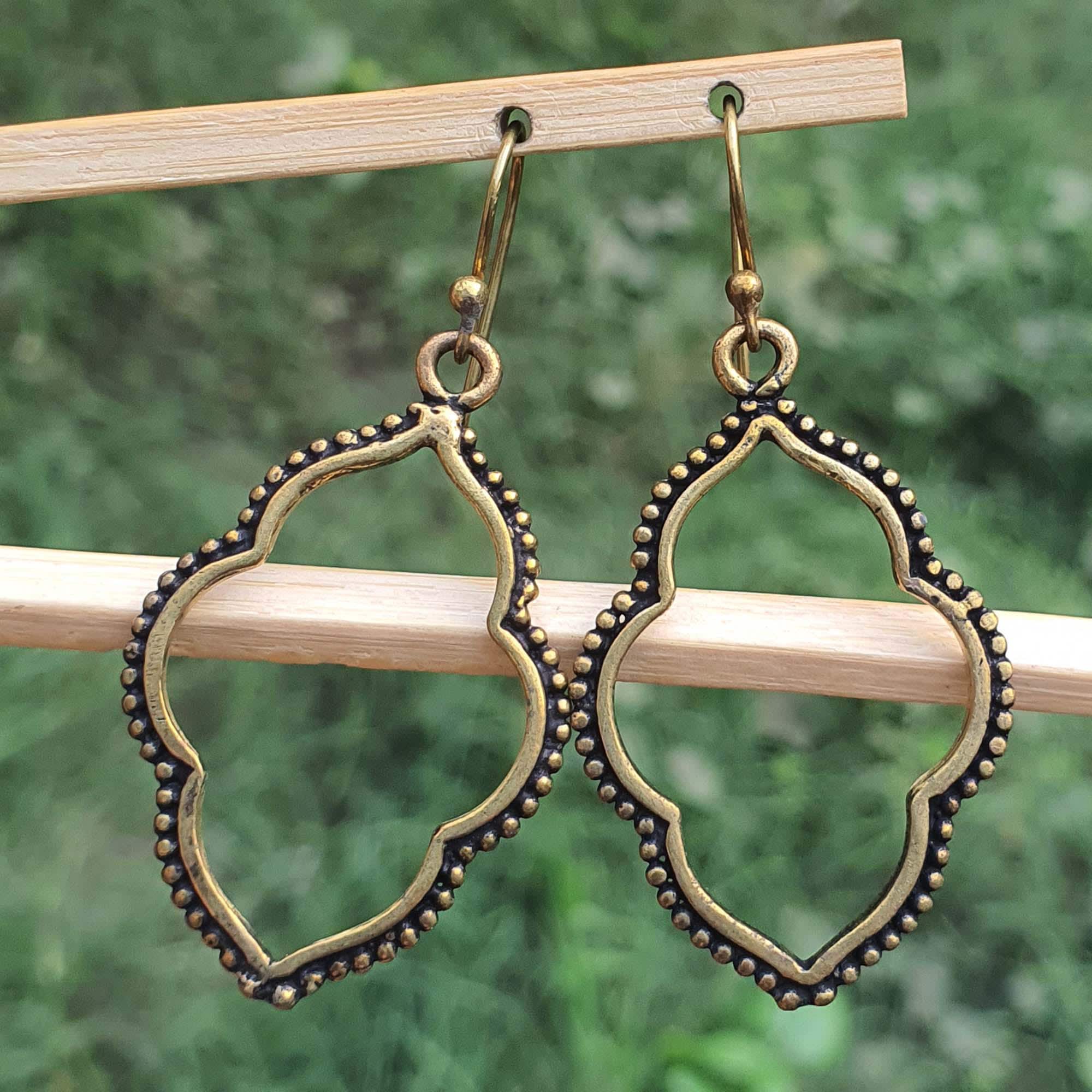 Pair of gold and black earrings hanging on a wooden stick with a green blurred background
