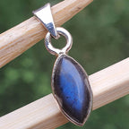 Blue stone pendant with silver setting on a wooden stick against a blurred green background