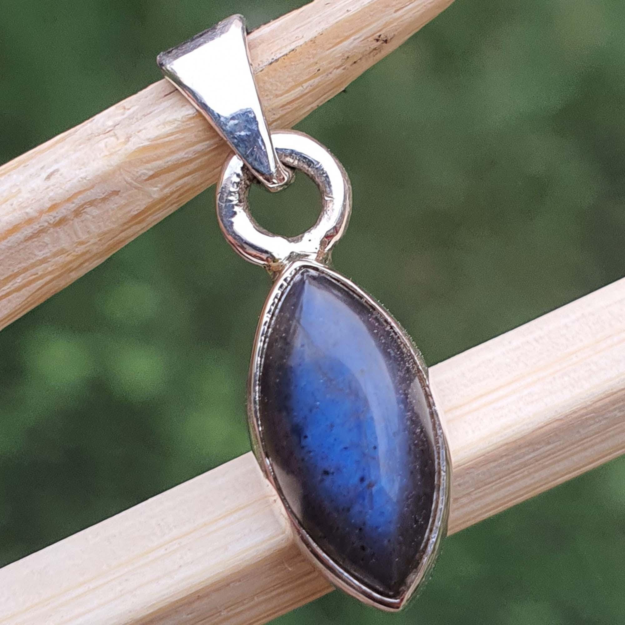 Blue stone pendant with silver setting on a wooden stick against a blurred green background