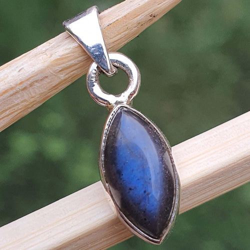 Blue stone pendant with silver setting on a wooden stick against a blurred green background