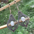 Ornate silver earrings with white stones on a wooden stick against a blurred green background