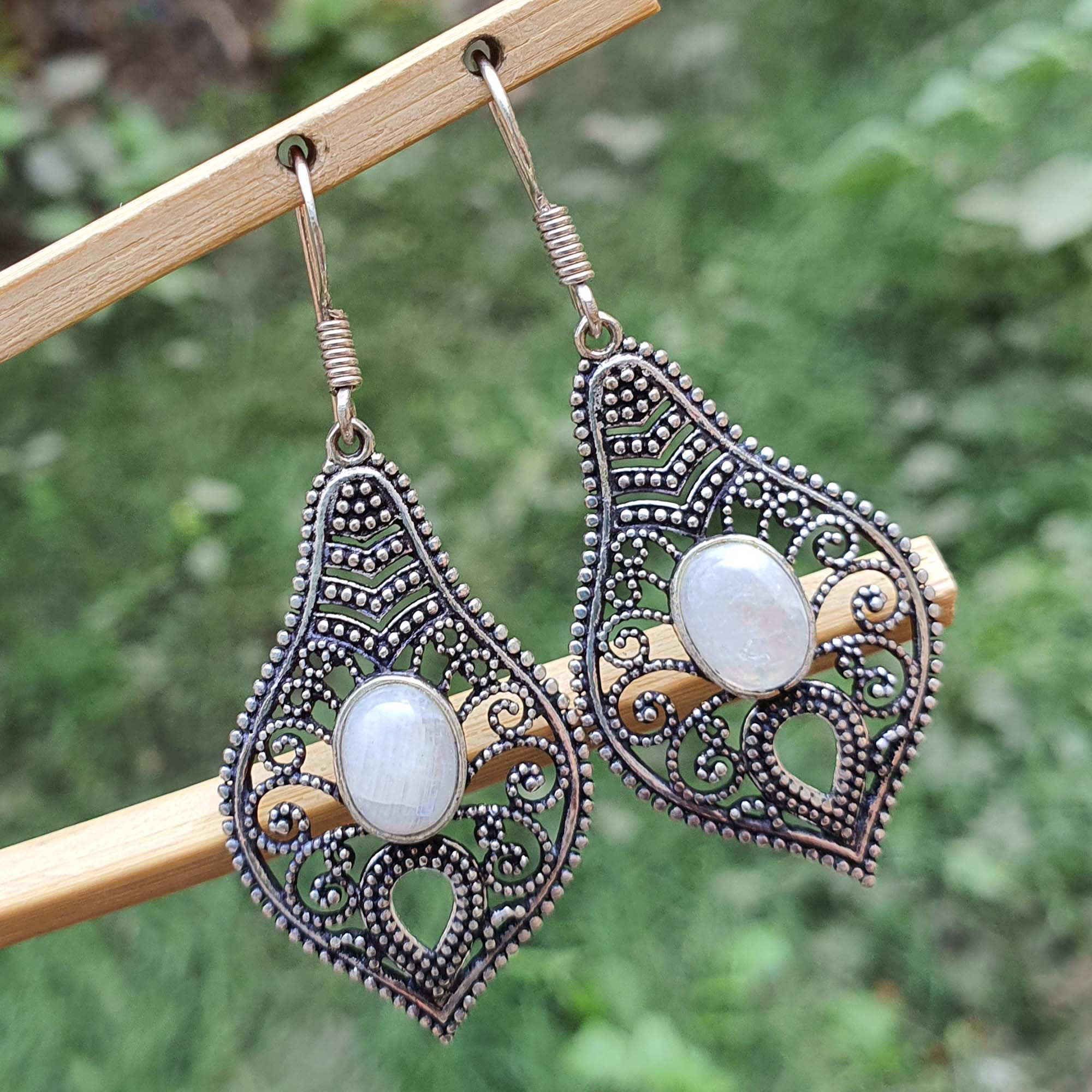 Ornate silver earrings with white stones on a wooden stick against a blurred green background