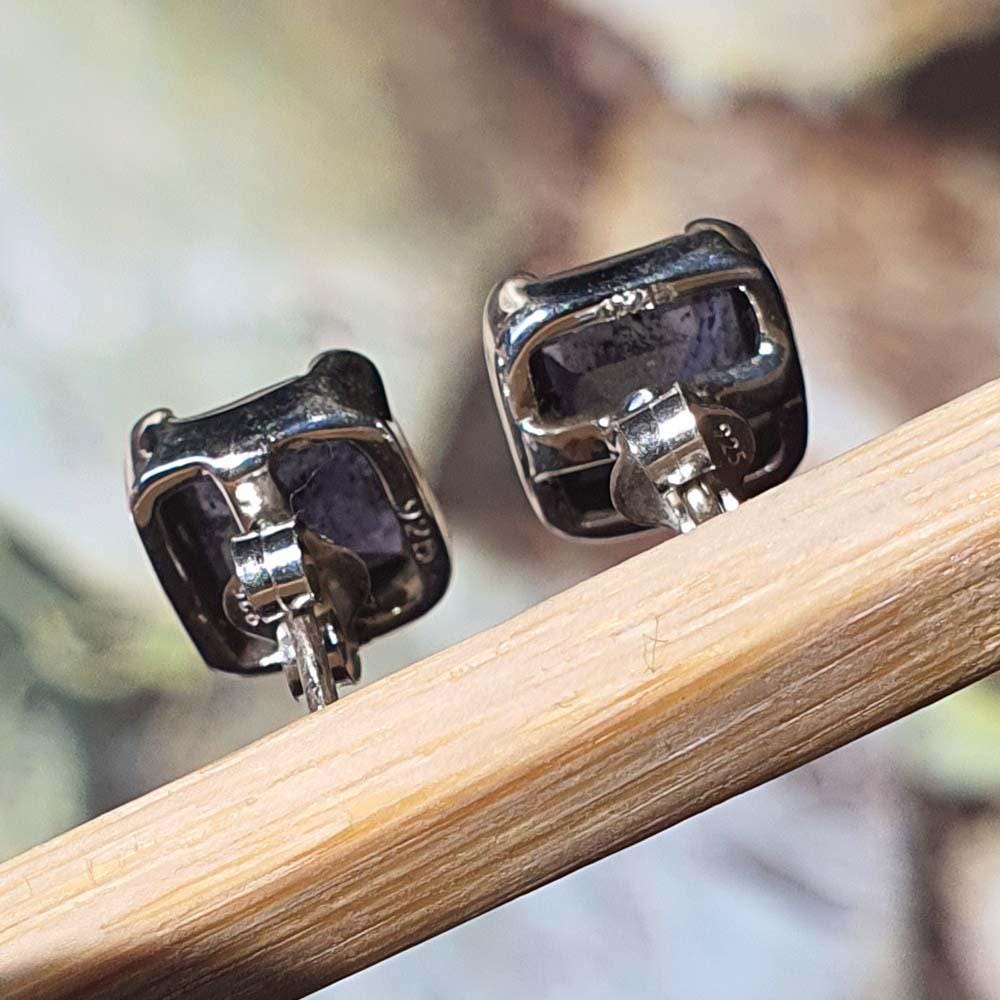 Pair of silver square earrings with purple stones on a wooden stick against a blurred natural background