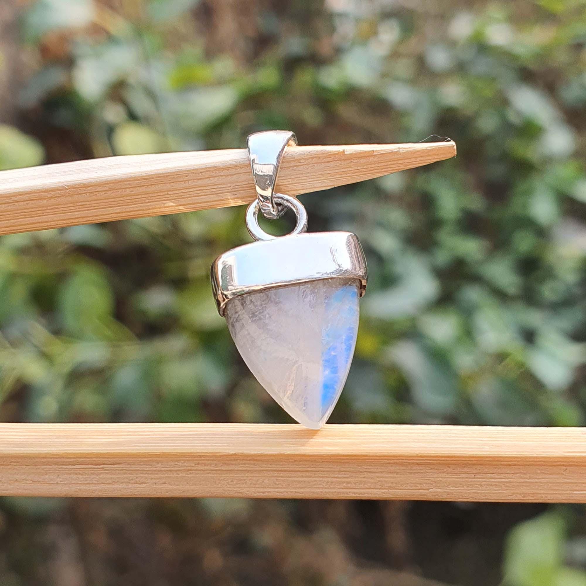 Pendant with a rainbow moonstone on a wooden stick against a blurred green background