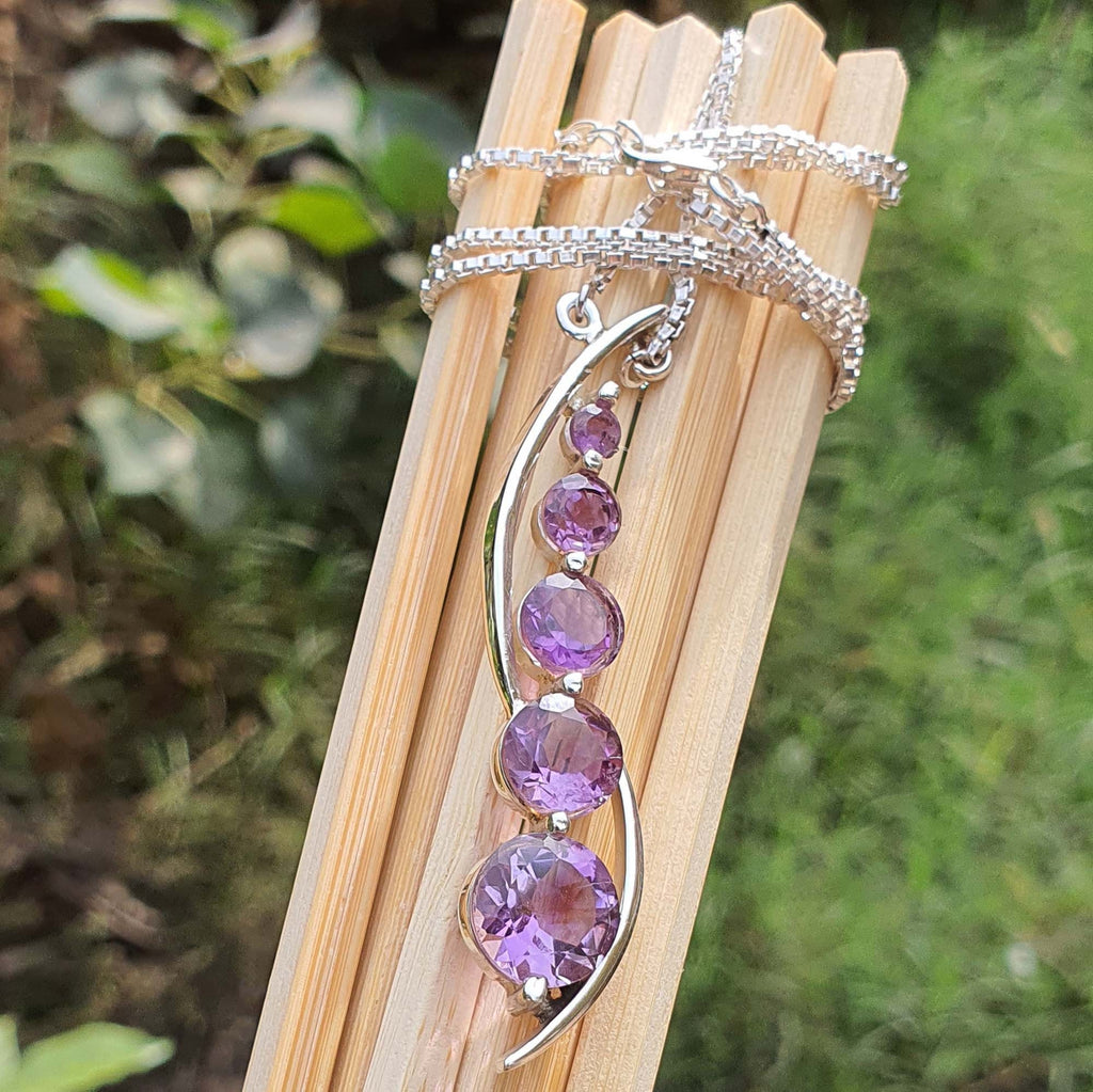 Silver necklace with purple gemstones on a wooden stick against a natural background
