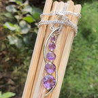 Silver necklace with purple gemstones on a wooden stick against a natural background