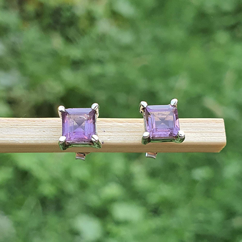 Pair of square purple gemstone earrings on a wooden stick with a green blurred background