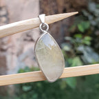 Teardrop-shaped pendant with a silver setting on a wooden stick against a natural background