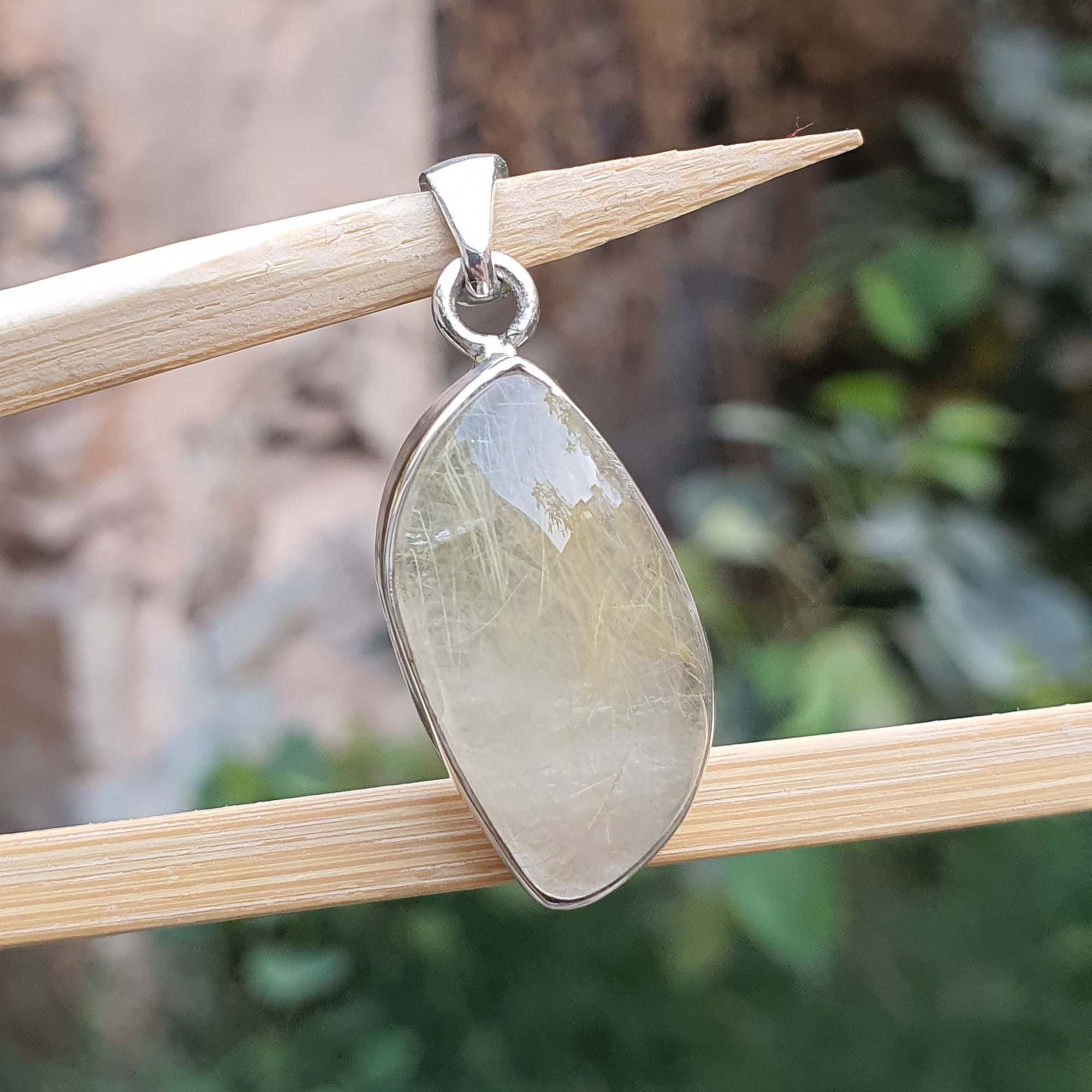 Teardrop-shaped pendant with a silver setting on a wooden stick against a natural background
